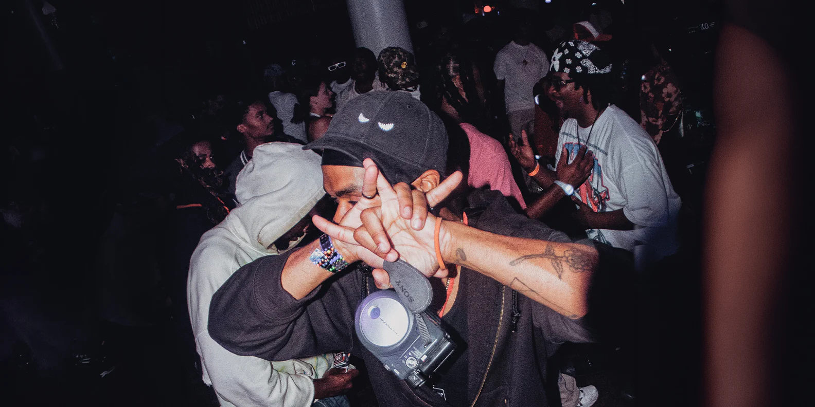 A crowd at a Madclub night, one guest in a Madcap throwing a hand sign